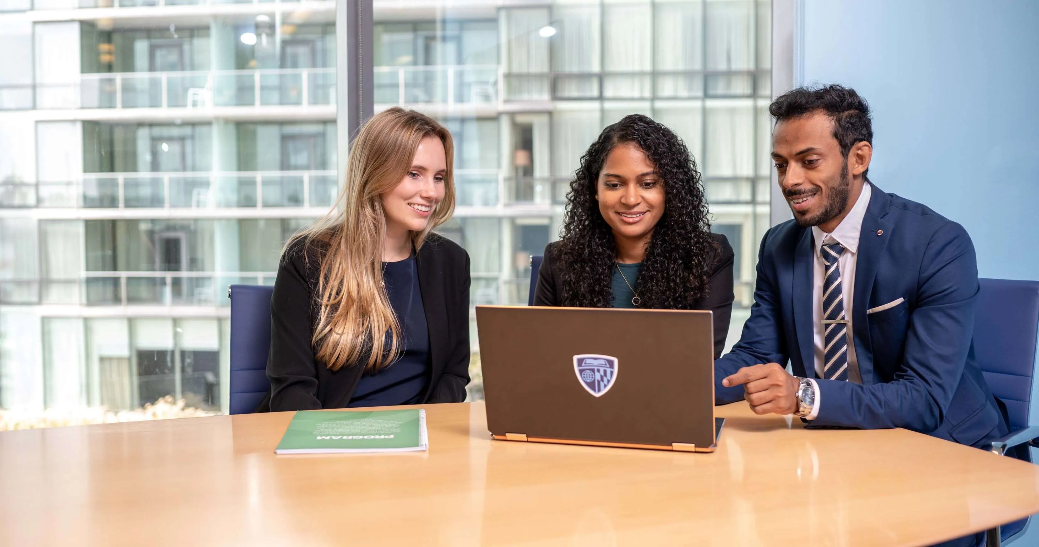 three people sitting at a table with a laptop