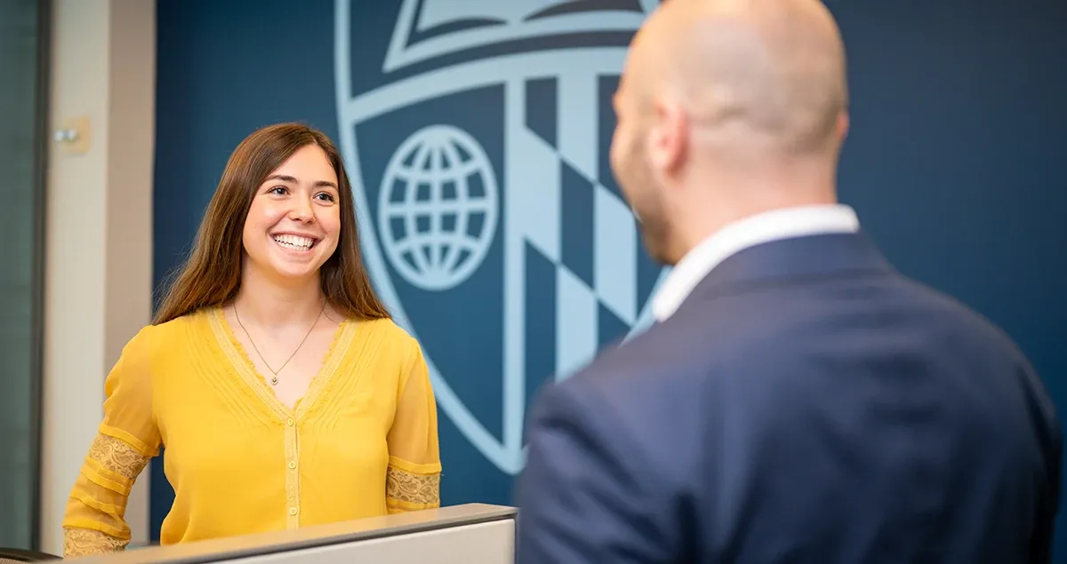 Two student talking in front of a University shield. 