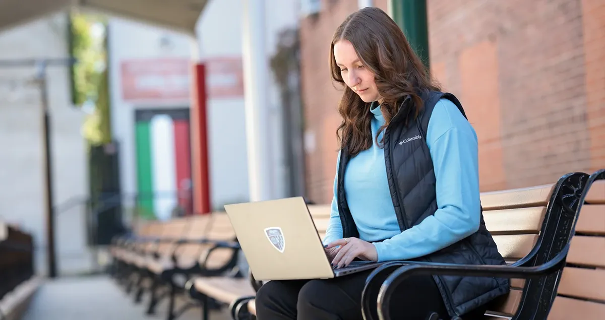 Student working on computer sitting on bench outside