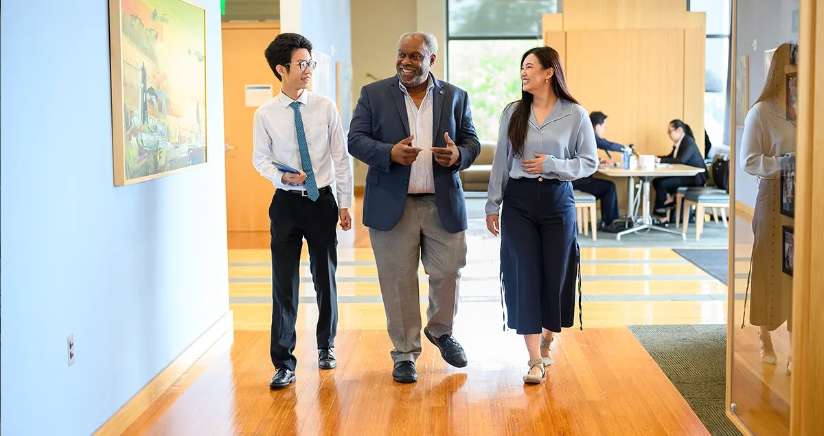 Two students walking in hallway with a faculty member. 