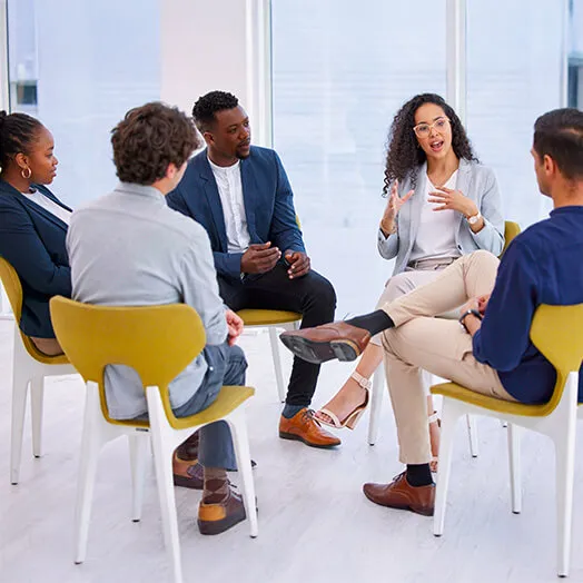 Several people seated in a discussion group with a woman saying something of interest