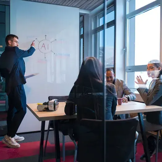 student team session with 3 seated and one standing pointing to AI on the white board