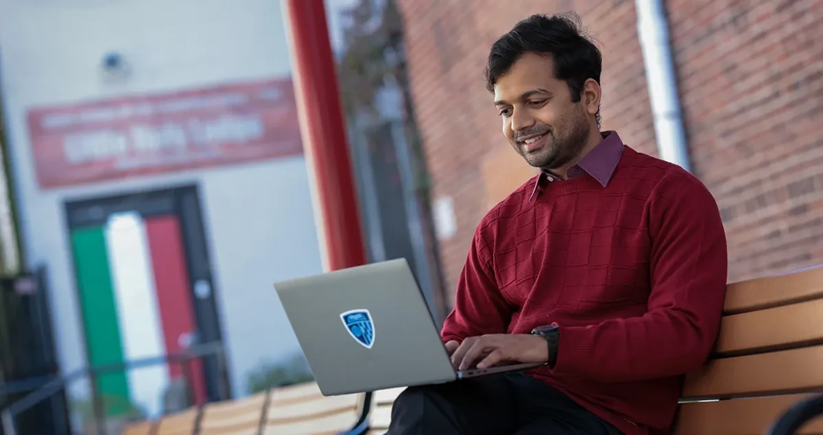 Student working on a computer outdoors sitting on a bench