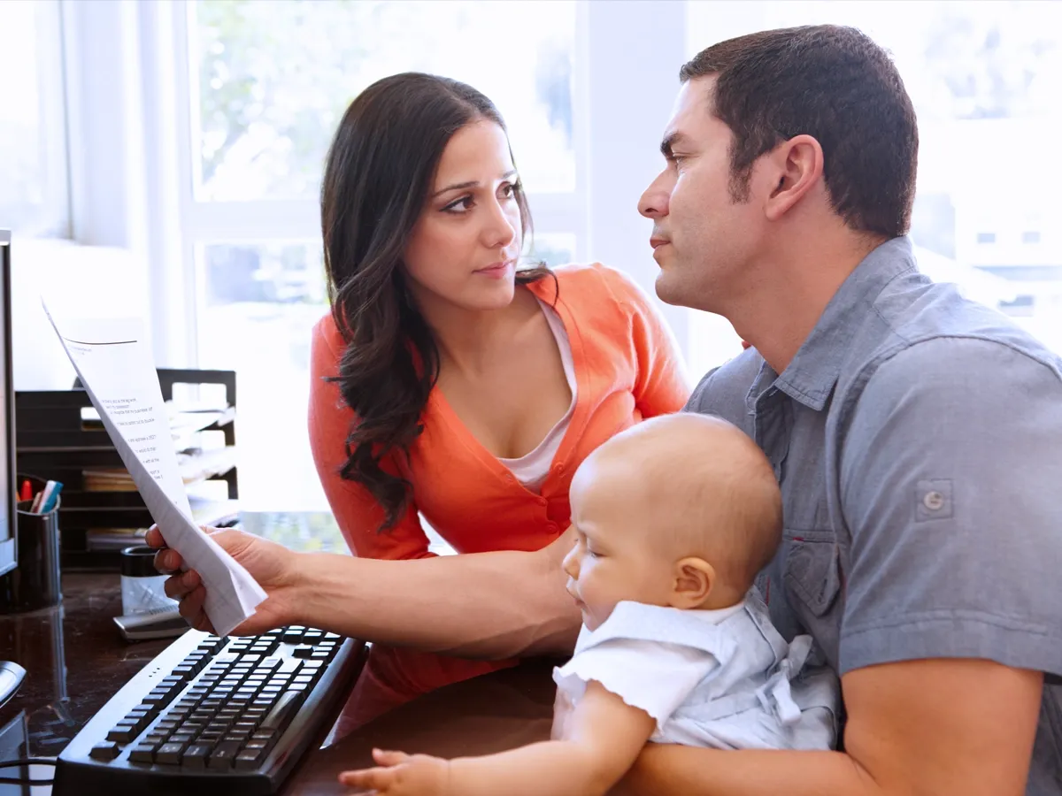 Man working on computer with baby in lap and woman sitting next to him.