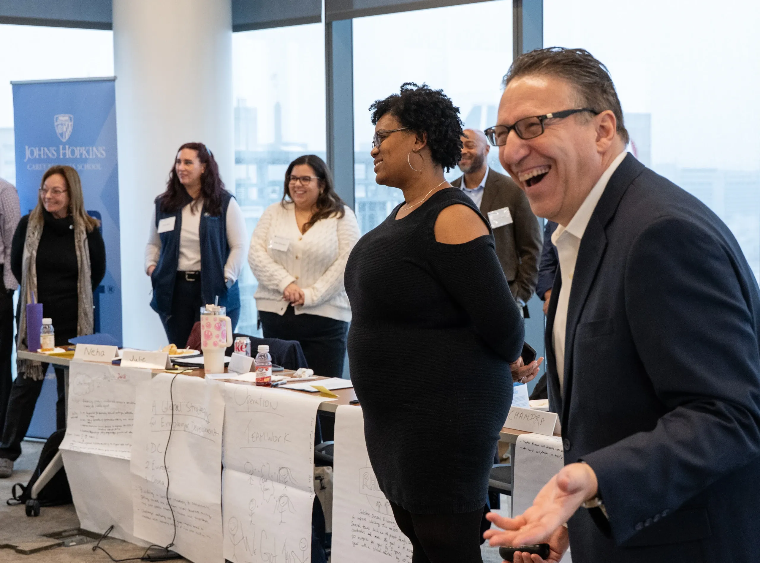 Johns Hopkins Carey Business School participants laugh and engage in a collaborative classroom activity with group notes displayed on tables.