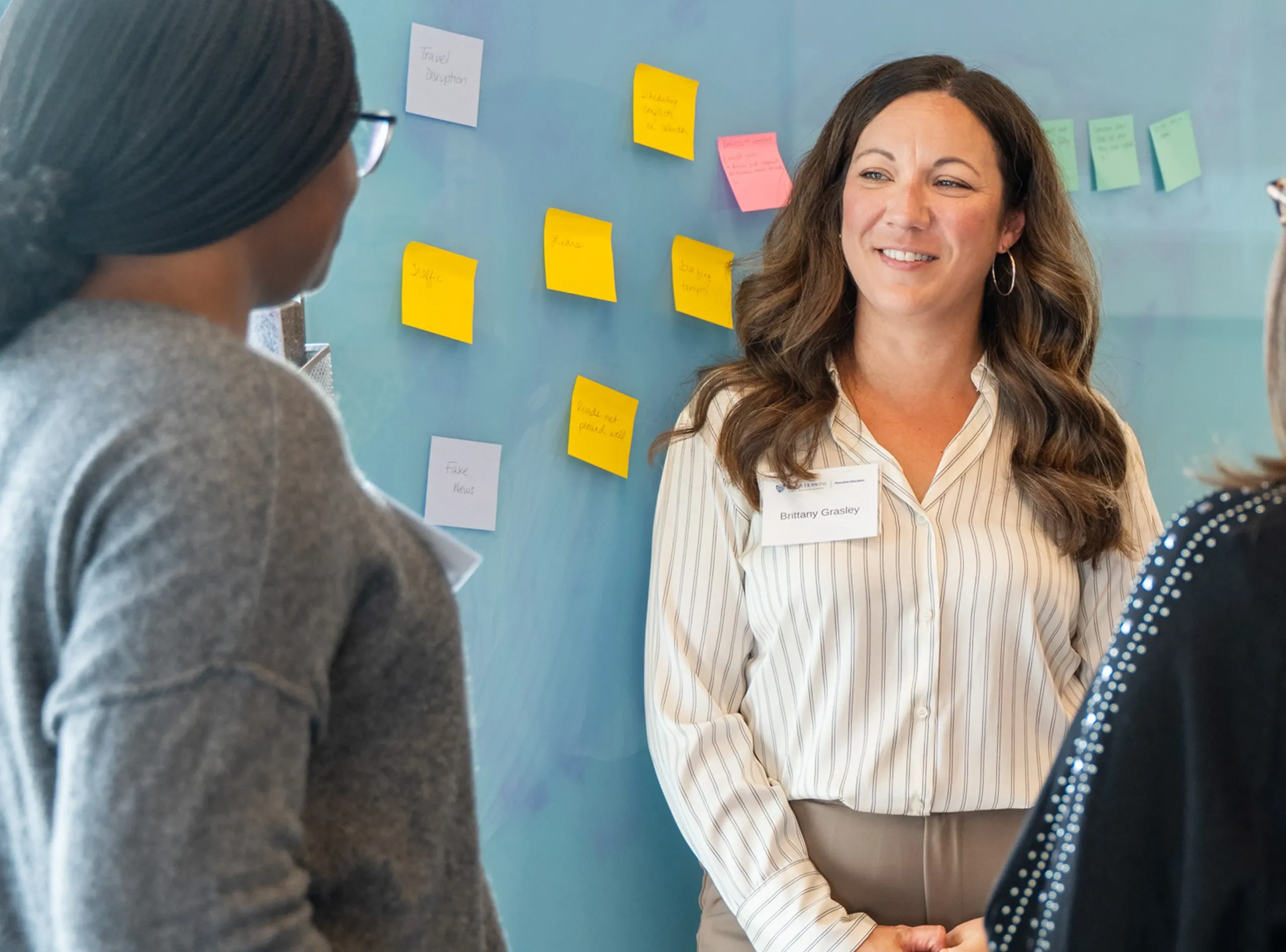 Two women participate in a design thinking facilitation session, standing near a glass wall covered with sticky notes.