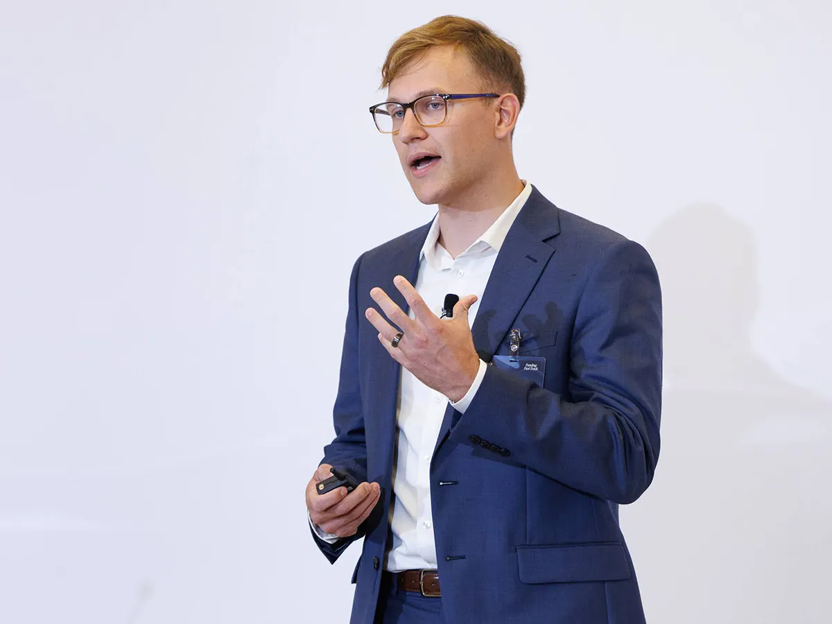 Man in navy suit and glasses speaking and gesturing during a presentation