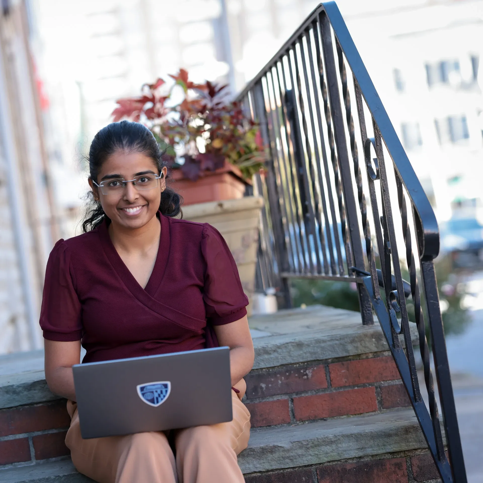 Smiling woman with glasses using a laptop on outdoor steps by a railing