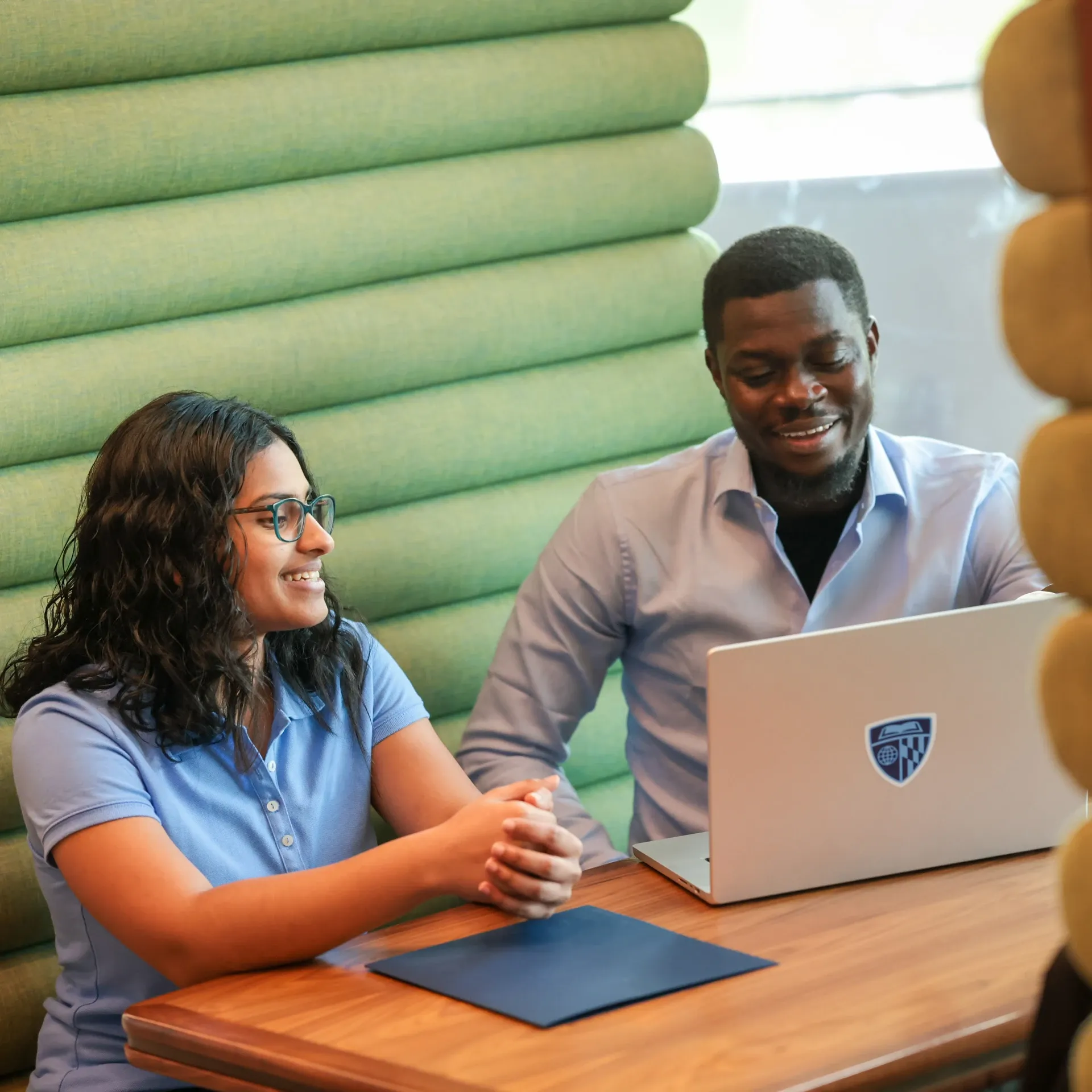 Two coworkers smiling at a laptop during a meeting in a modern office