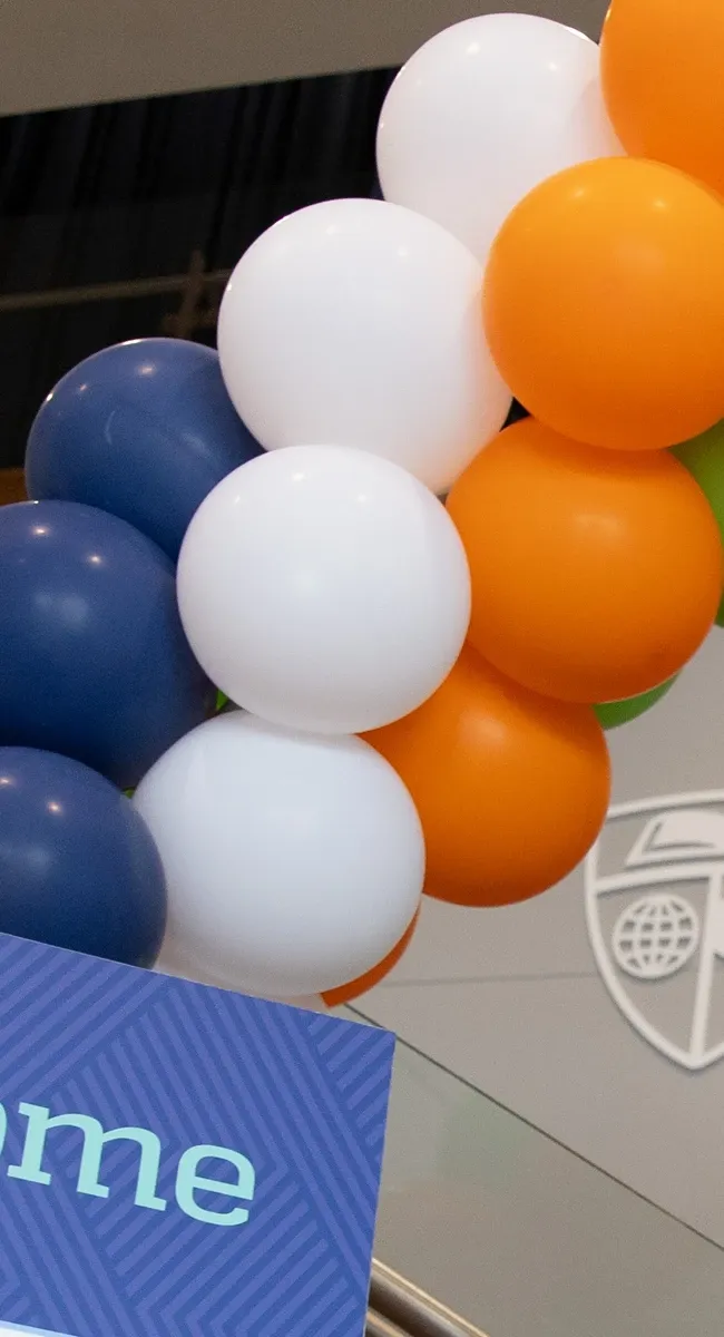 Blue, white, and orange balloon arch above a sign reading “Welcome”