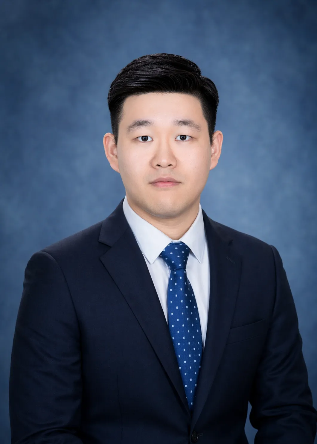 Studio portrait of man in navy suit and blue tie against blue backdrop