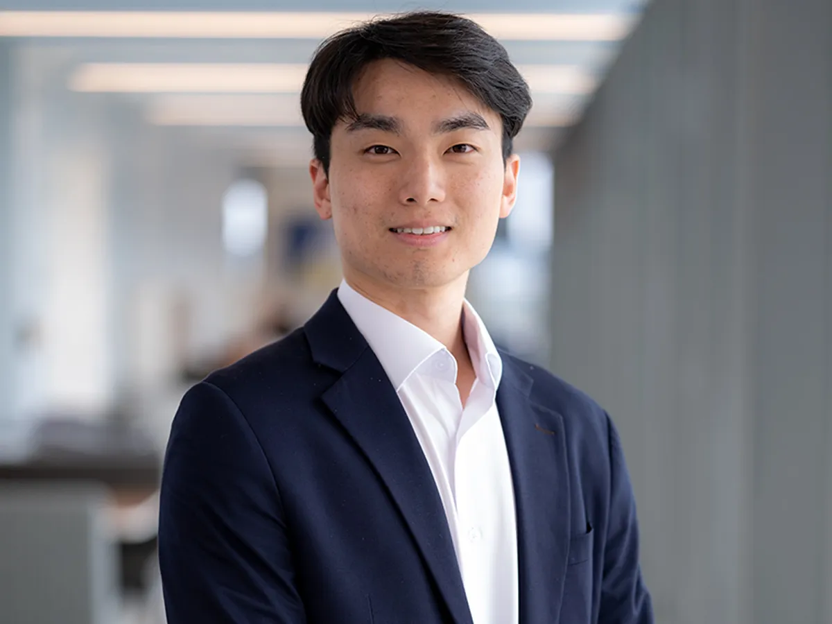 Smiling man in a navy suit standing in a bright office corridor