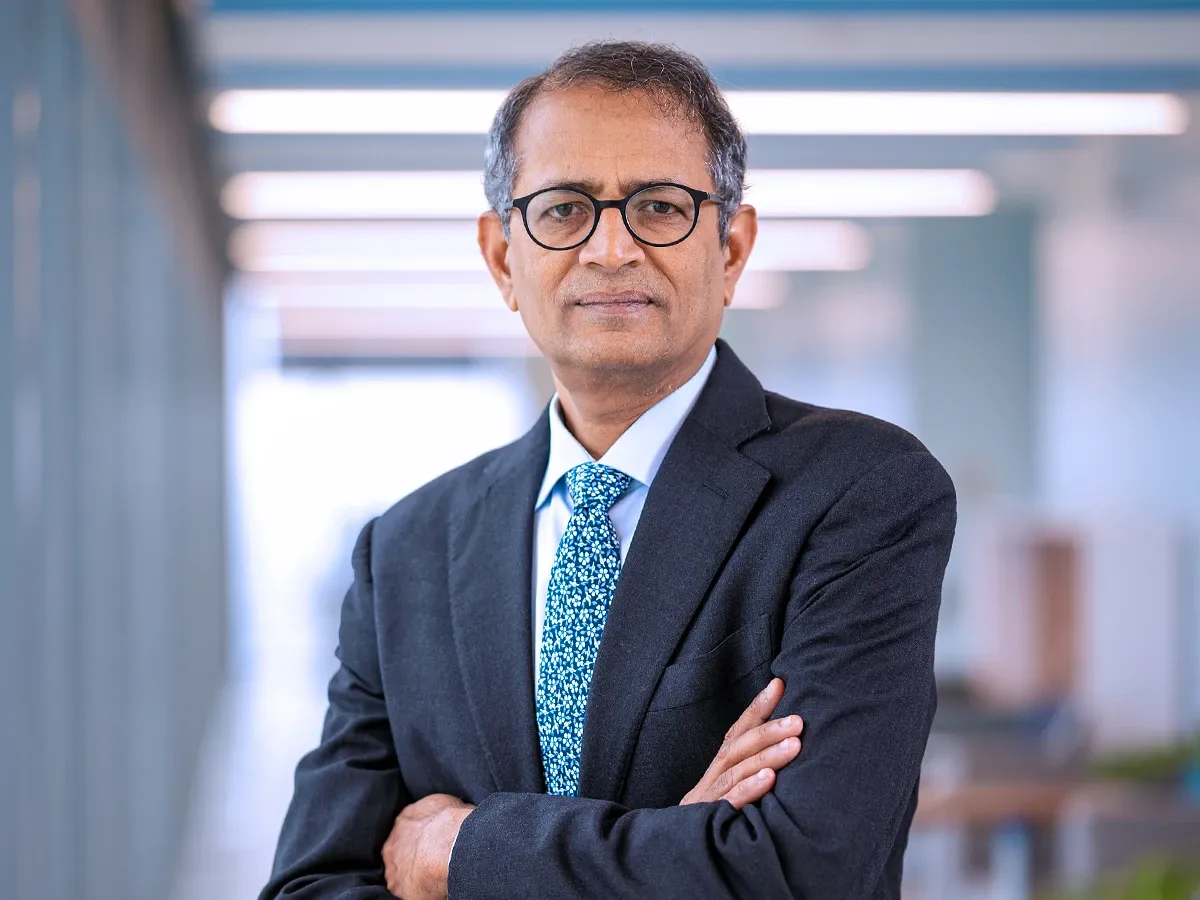 Businessman in suit and glasses, arms crossed, standing in a modern office corridor