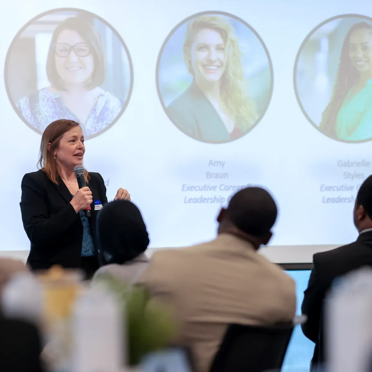 Woman speaking into microphone at business conference, audience in foreground