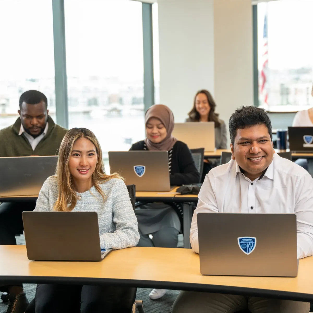 Students working on laptops in a bright classroom, smiling during a lesson