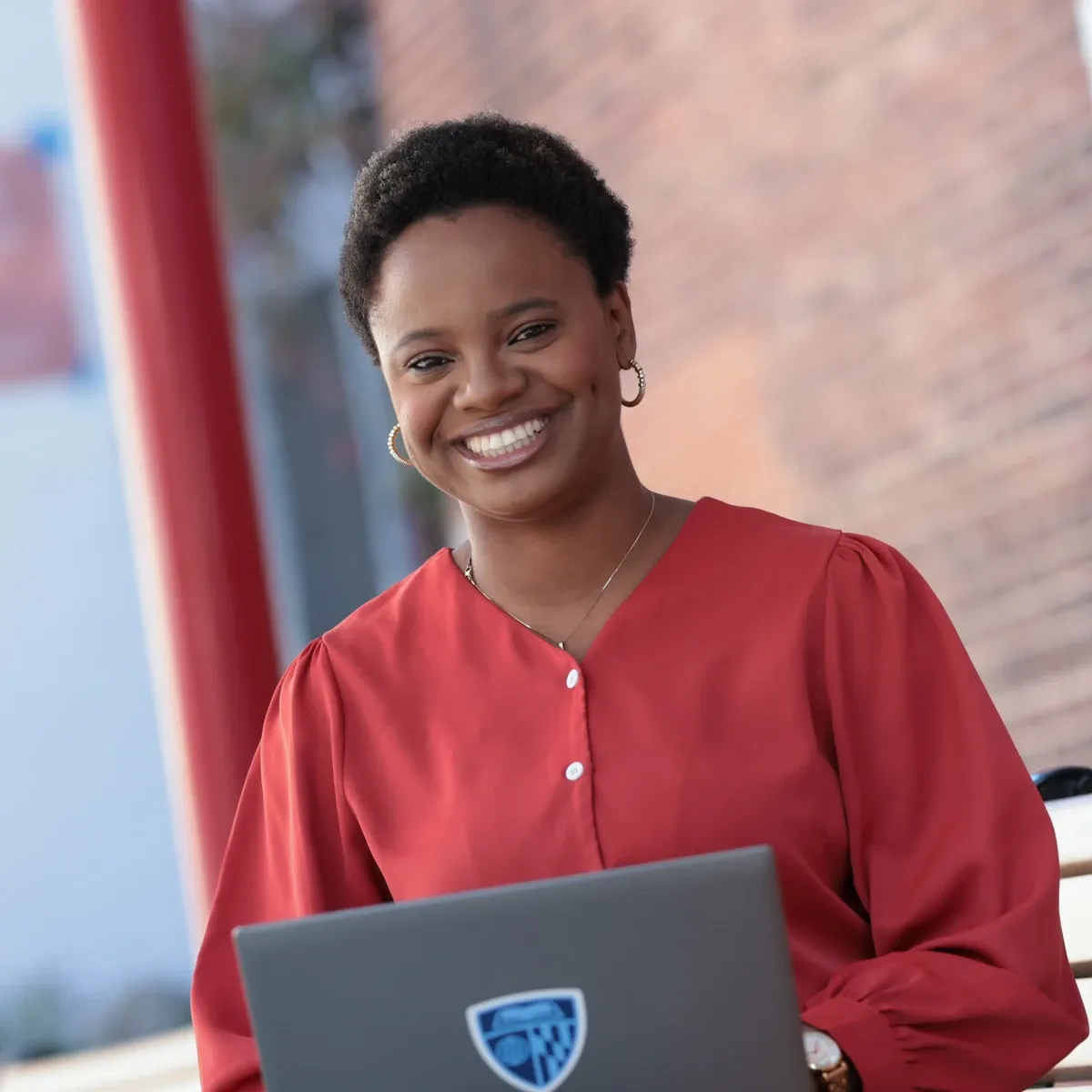 Smiling woman in red blouse using a laptop outdoors