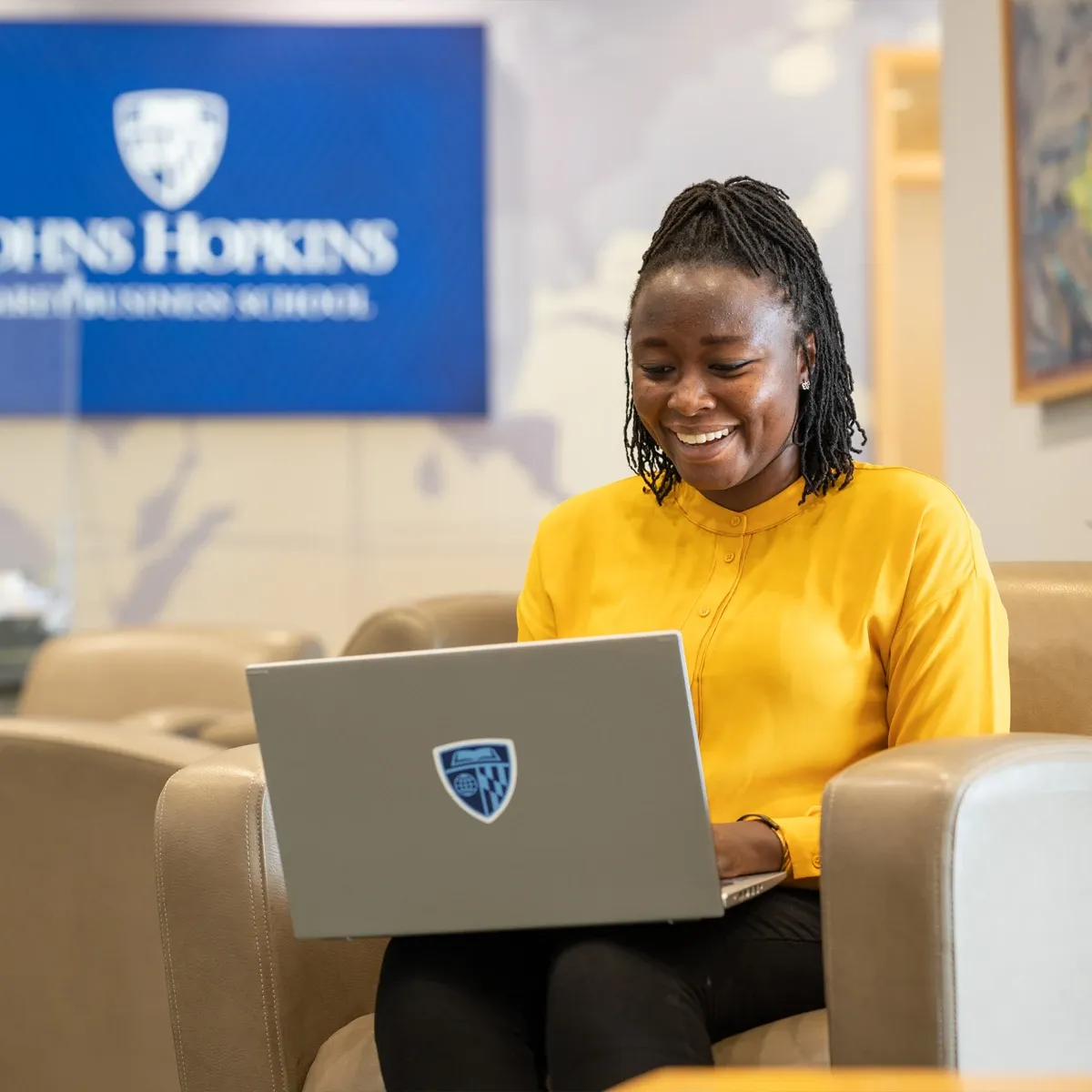 Smiling woman in yellow sweater using laptop at Carey 
