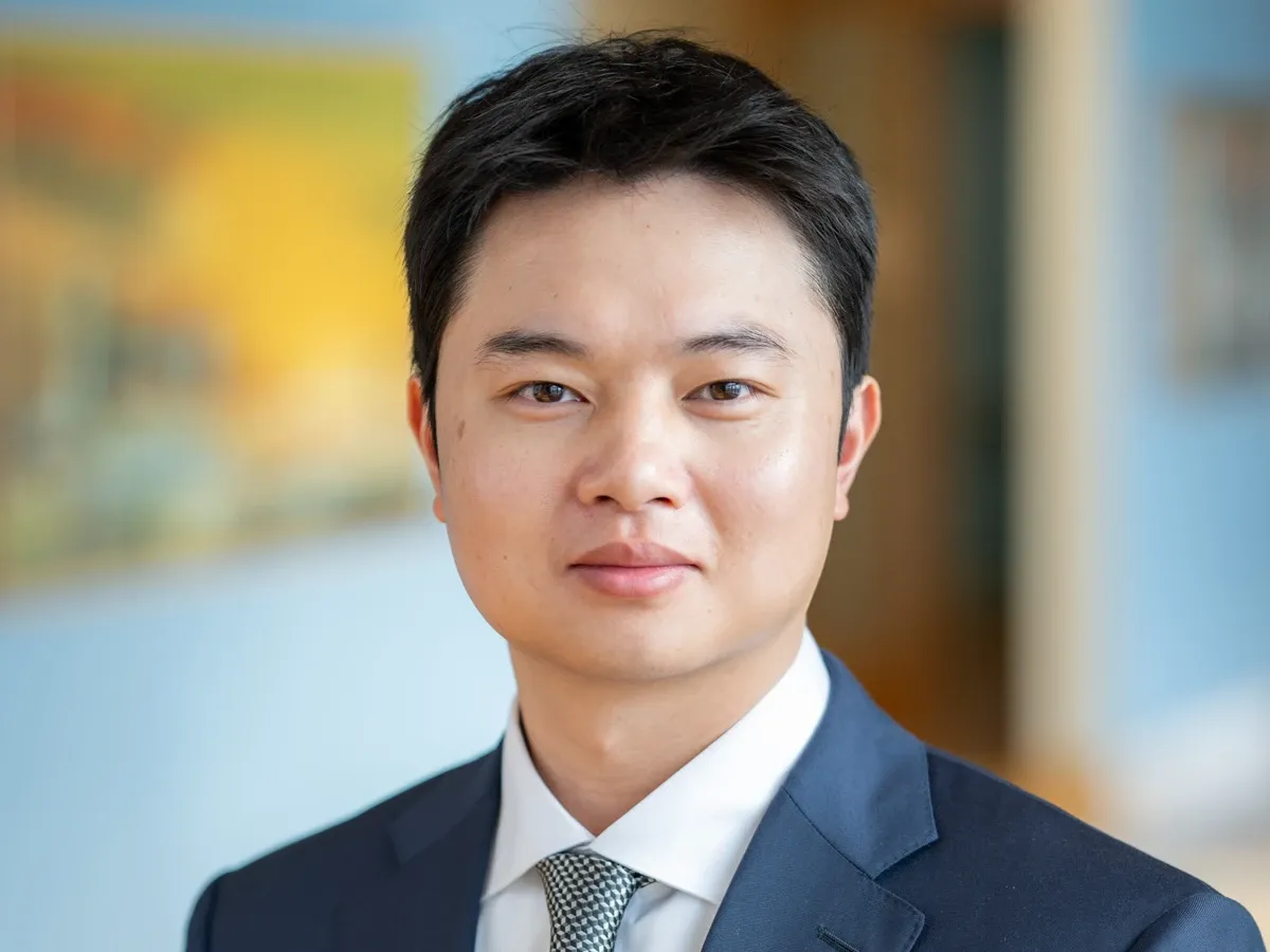Headshot photo of a man in a suit and tie, softly blurred office background