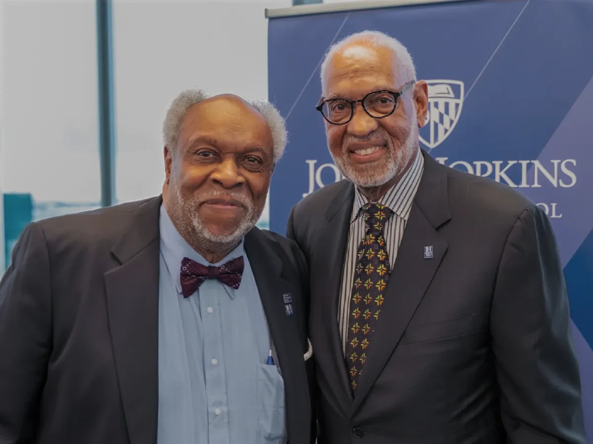 Two men in suits smiling together at an event backdrop