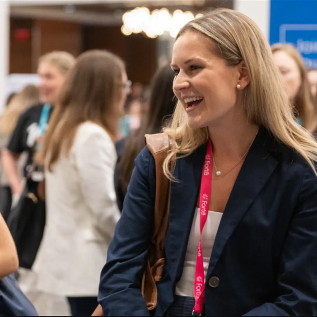Smiling blonde woman in navy blazer with pink lanyard at Forté Forum conference