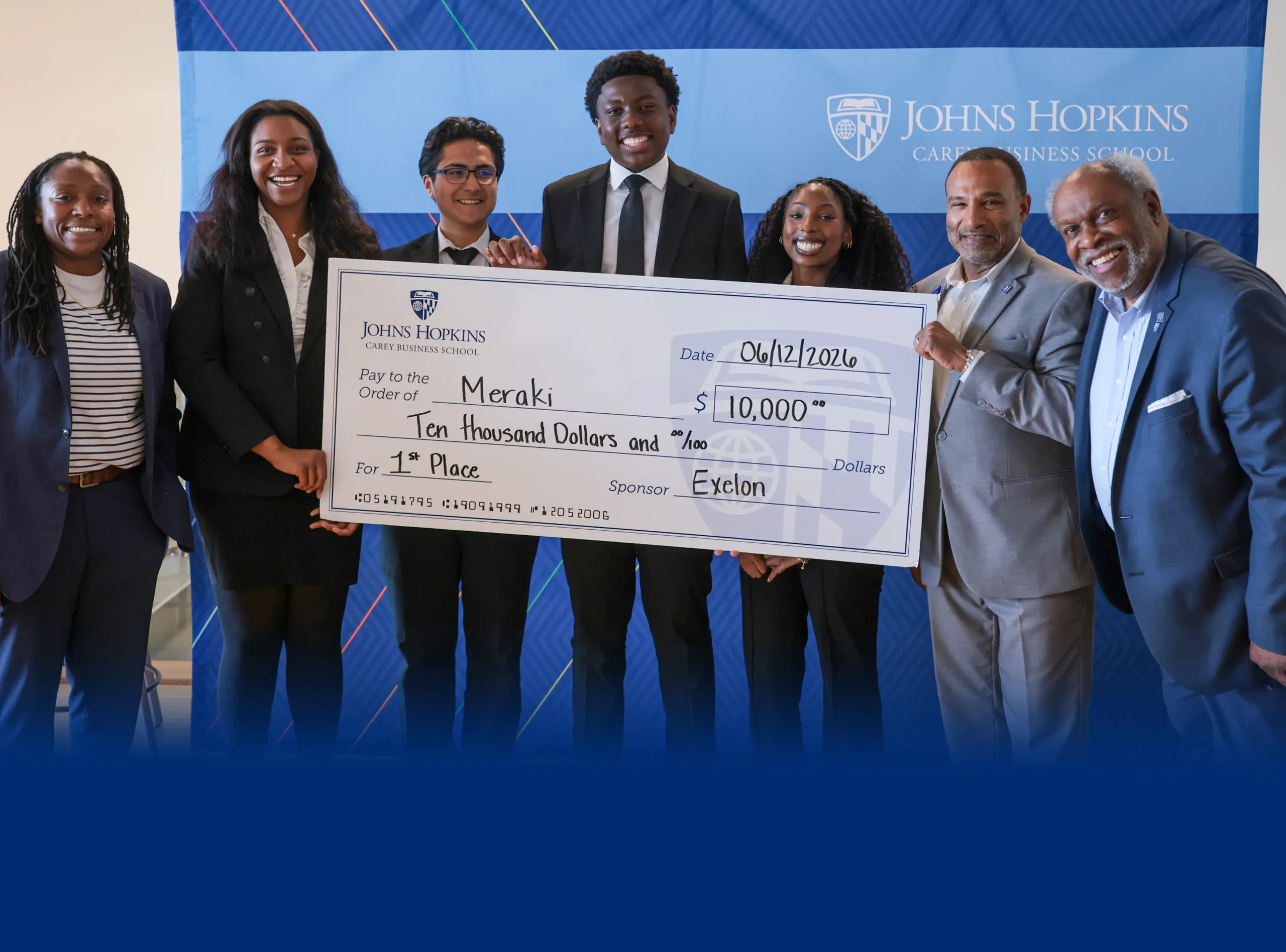 Group holds oversized $10,000 check at Johns Hopkins awards event, smiling.