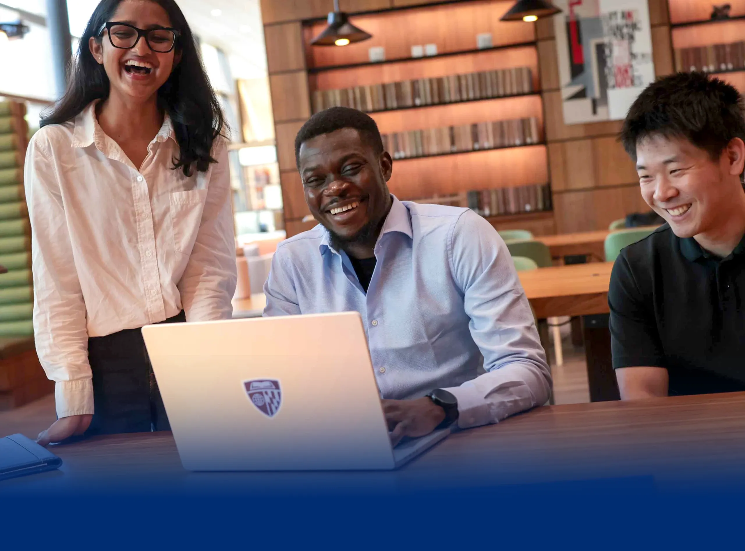 Three students smiling around a laptop in a bright office