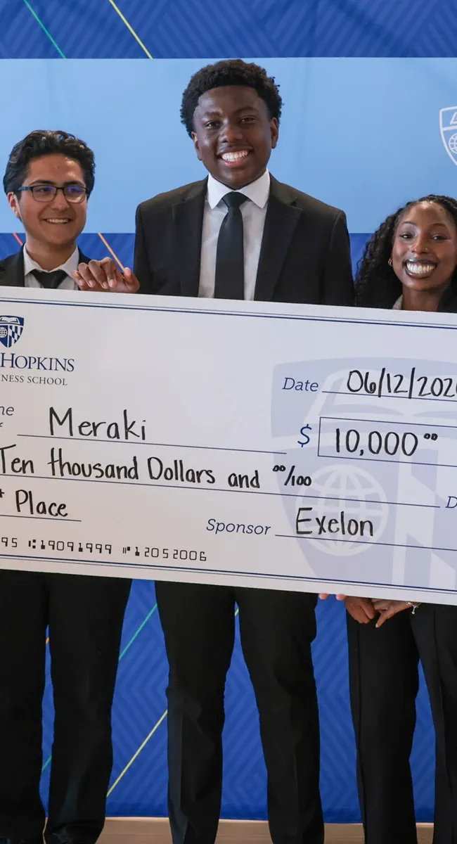 Three smiling people hold oversized $10,000 check at event backdrop