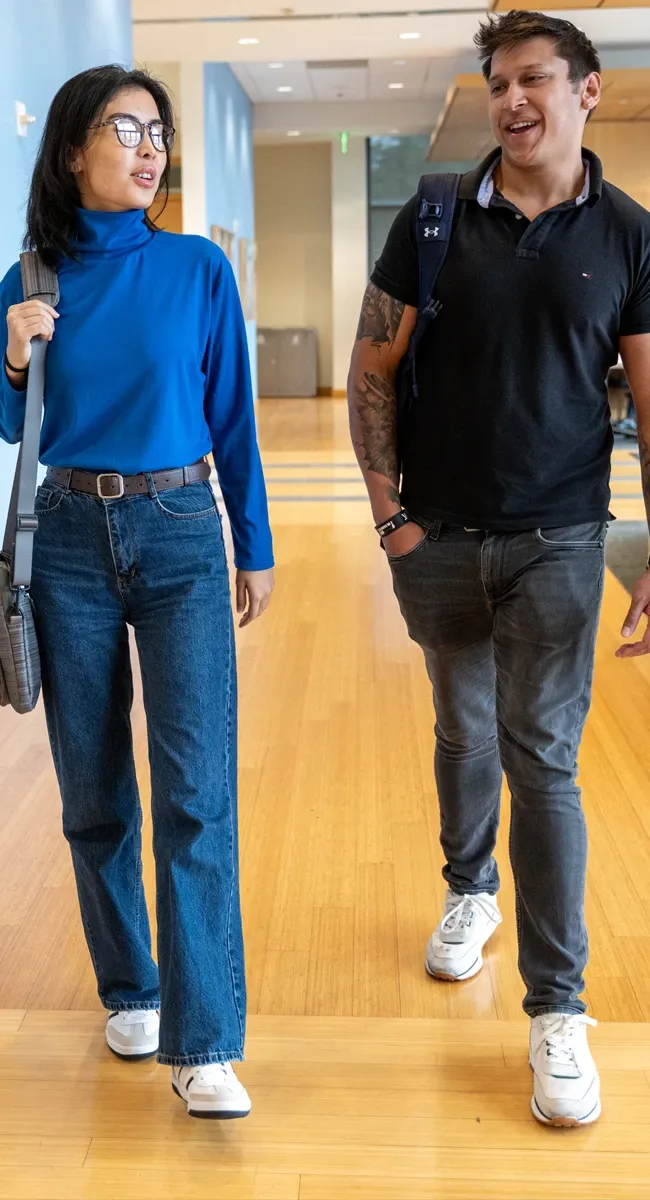 Two students walking and chatting in a bright hallway, both carrying backpacks