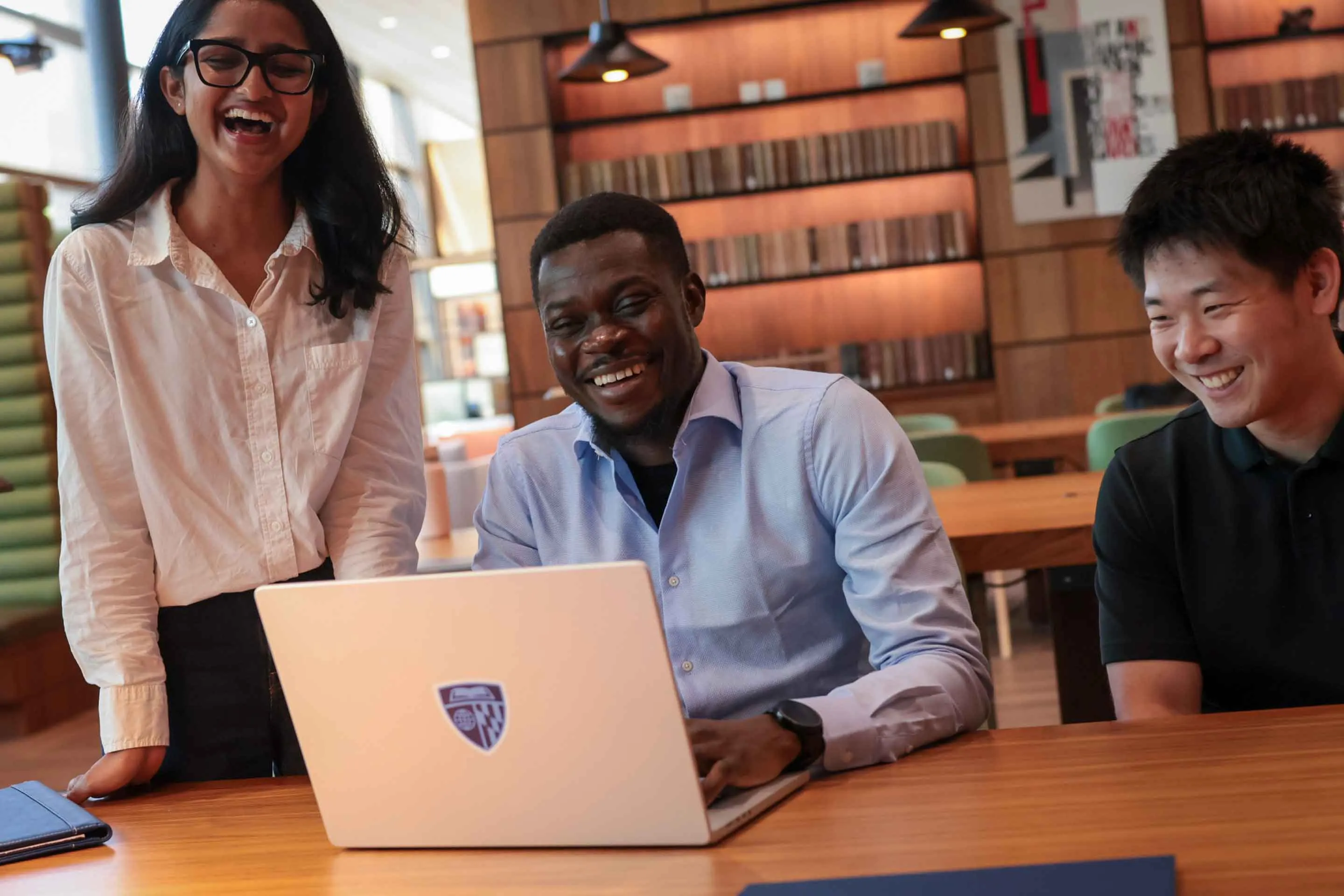 Students laughing with a computer at a desk in the library