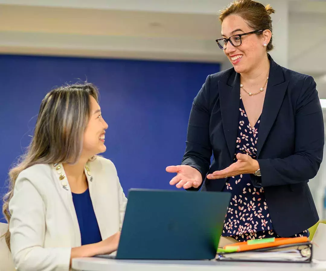 Faculty member explaining to a seated student with a laptop