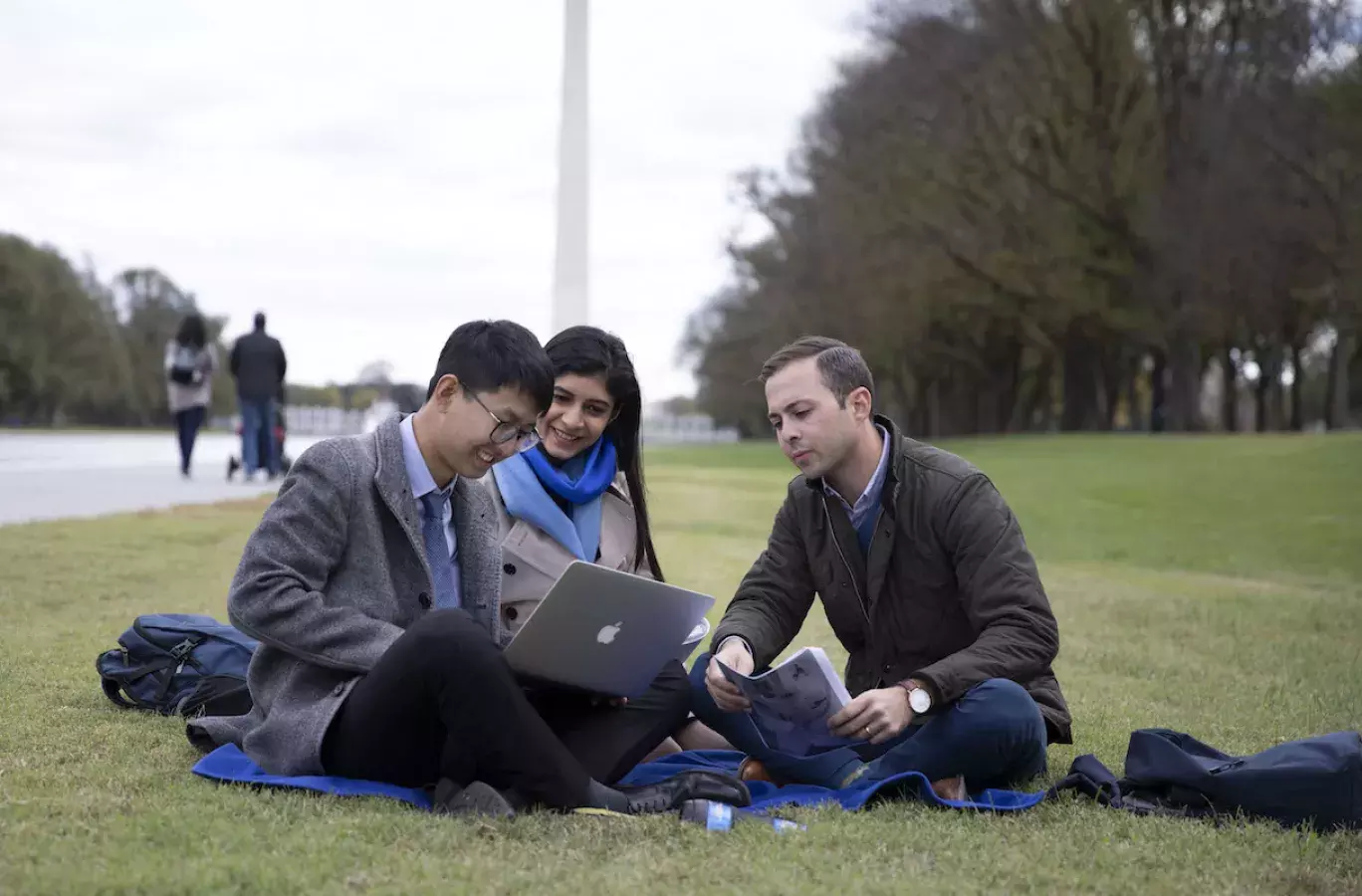 3 students siting on lawn in front of the Washington monument.