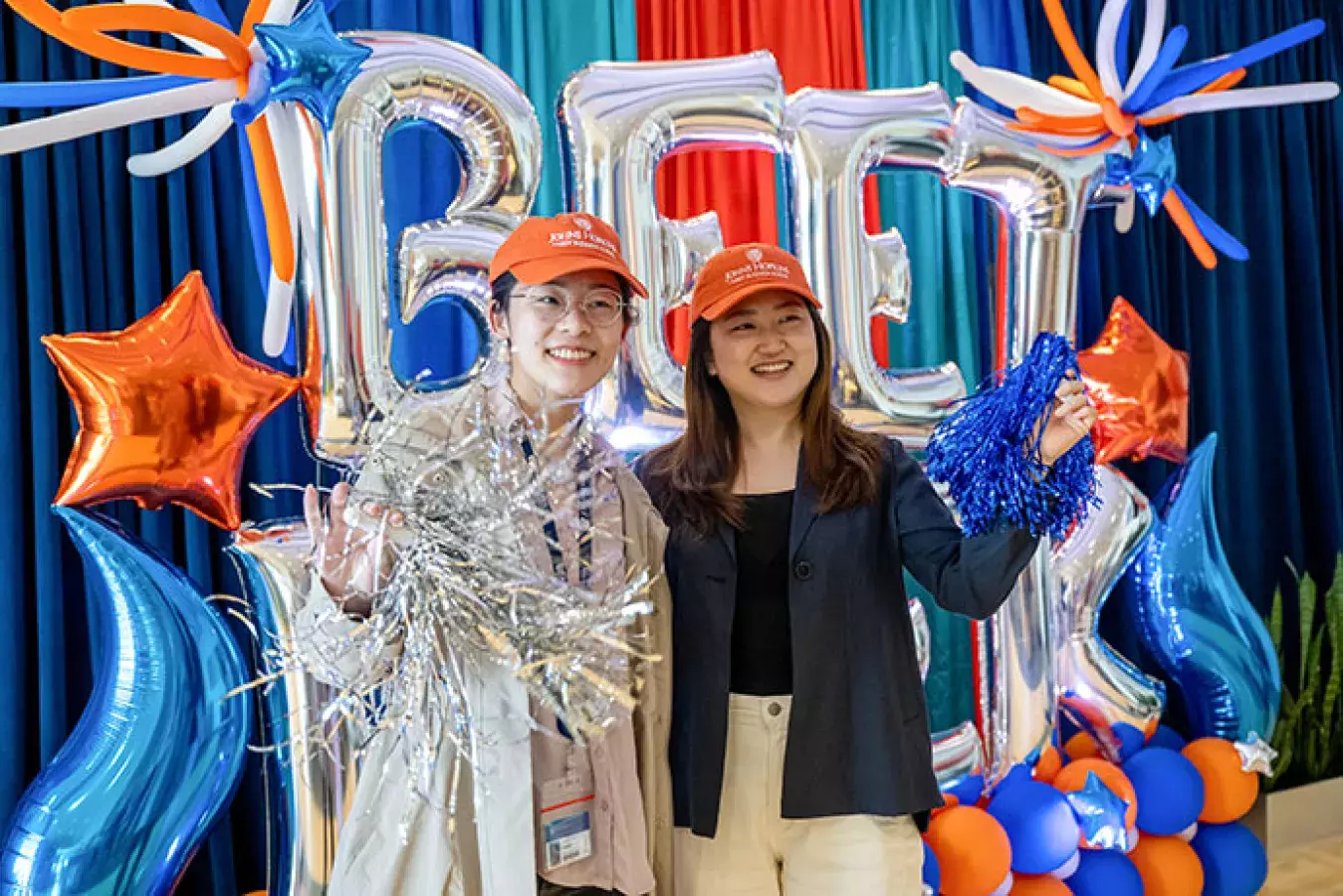 two JHU Carey Business School students waving pom poms standing in front of balloons some shaped in word BEET WEEK