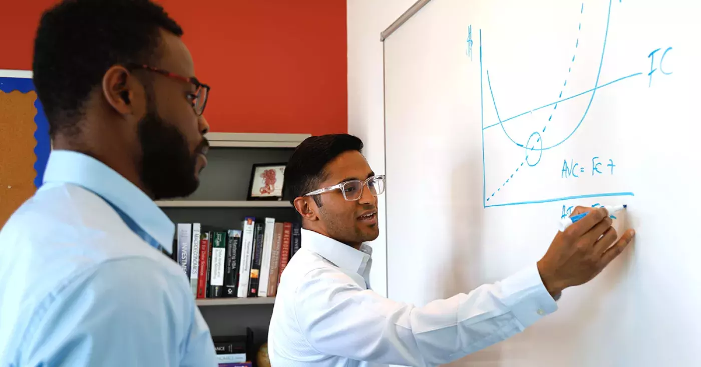 two people standing at a whiteboard with equations on it
