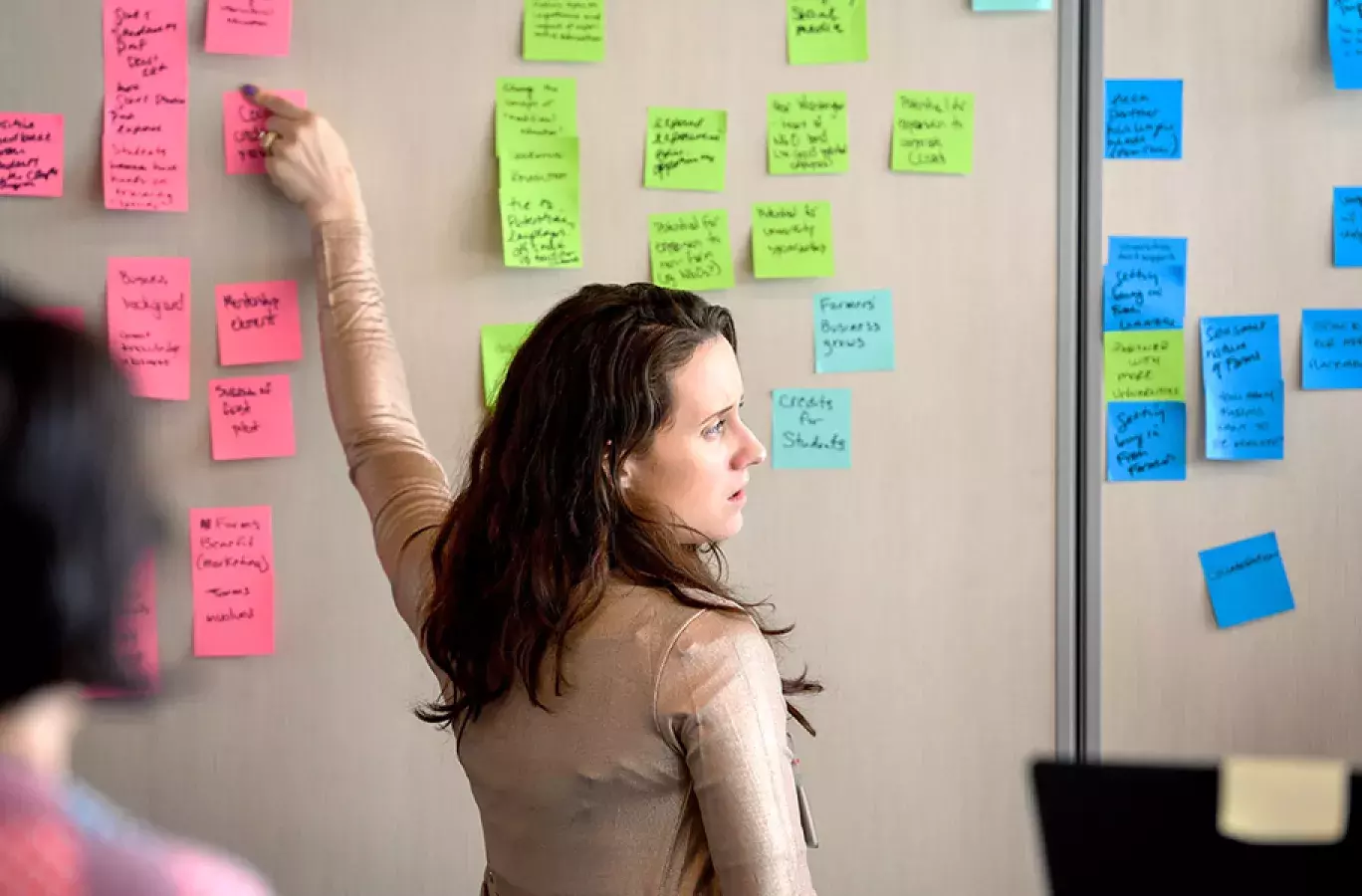 woman pointing to a sticky note on a board