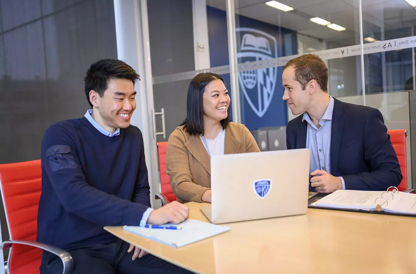 three students sitting at a table sharing a laptop