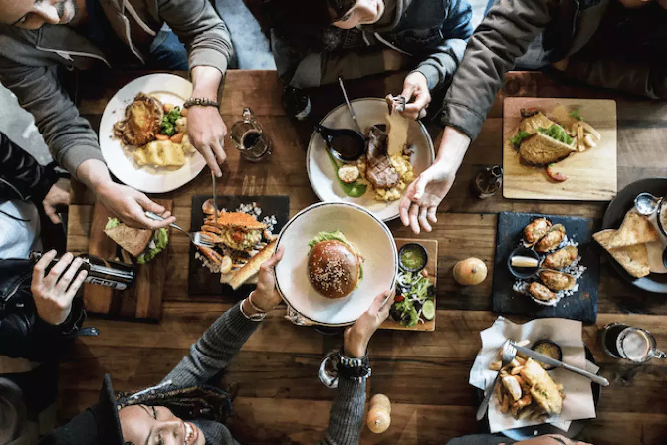 a group of seven people sharing a restaurant table with plates of food