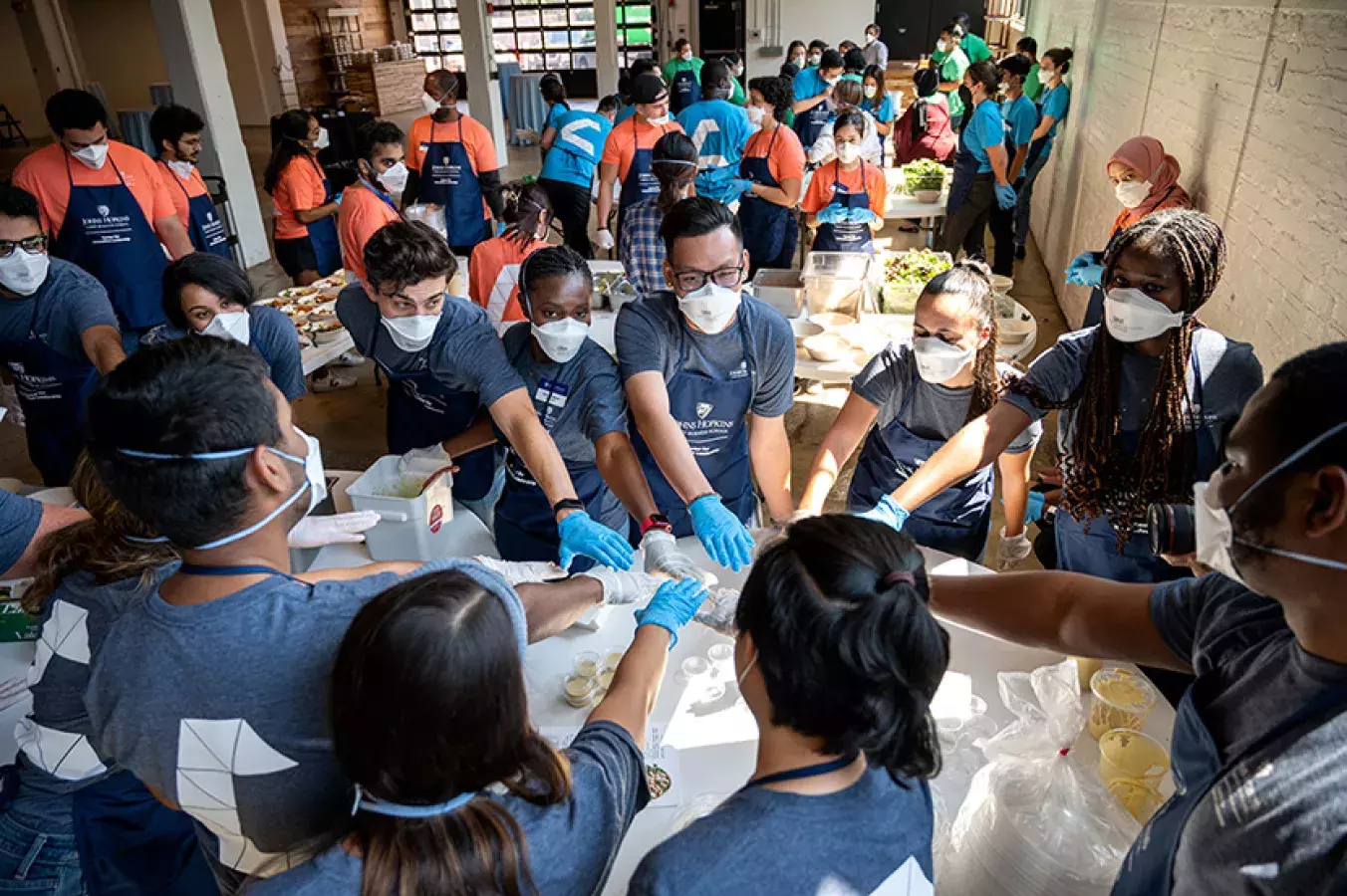 kitchen challenge with groups of teams wearing masks putting hands toward the center of a circular table