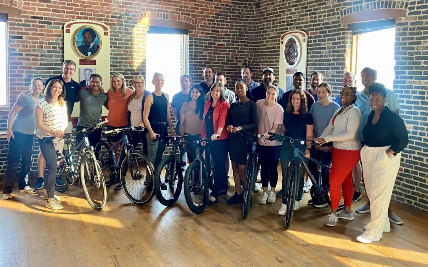 a group photo of 23 CIL residents with 6 bicycles in a brick walled and wood floor room.