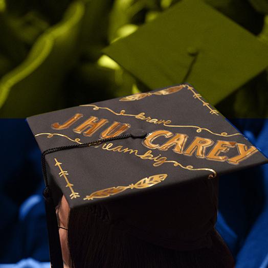 JHU Carey graduates with the picture frame filled by caps and one with embroidered saying brave JHU CAREY dream big