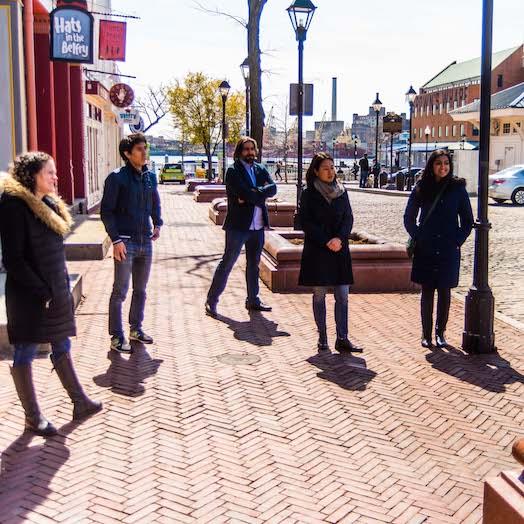 five students standing on a brick sidewalk in Fells point Baltimore listening to a professor