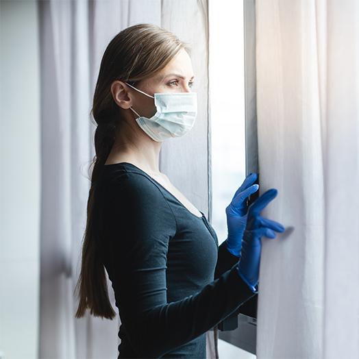 a women looking out of her window, wearing a mask while following social distancing measures in place during the COVID-19 pandemic in the United States