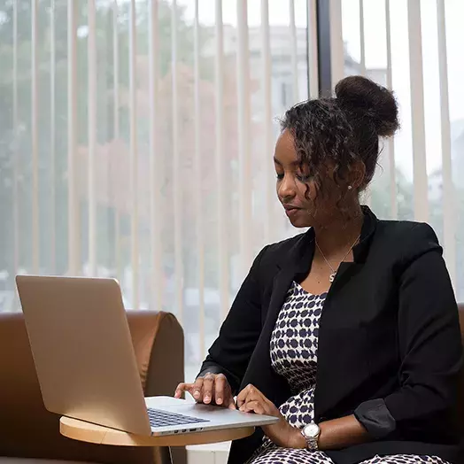 student sitting at a small round table in a Carey study area working on a laptop