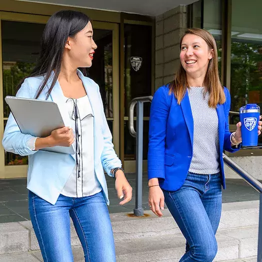 two studends walking downstairs chating while leaving the Carey Business school building