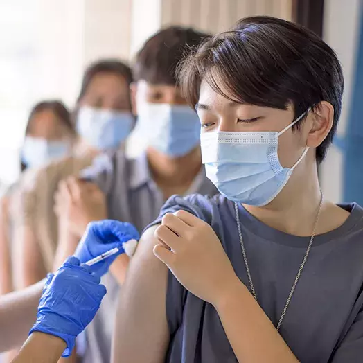 students waiting in a line while one is receiving a vaccine in the shoulder with a rolled up sleeve