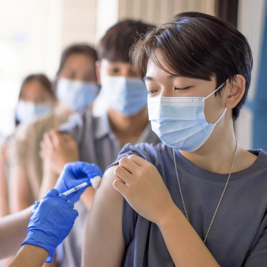 students waiting in a line while one is receiving a vaccine in the shoulder with a rolled up sleeve