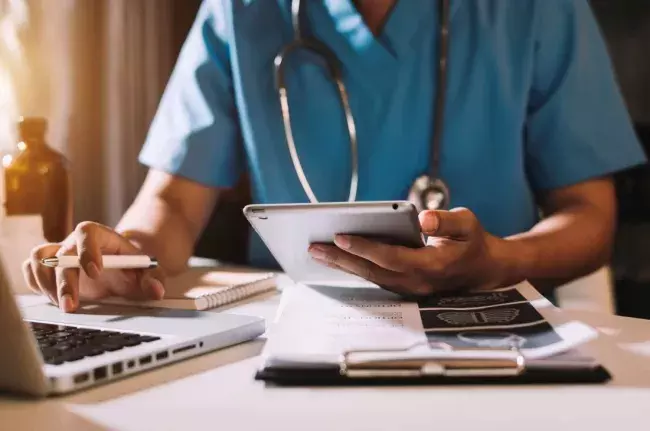 doctor in scrubs at laptop with tablet