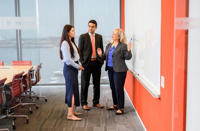 three people discussing in front of a white board