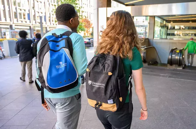 two students walking toward a transit escalator on a city street