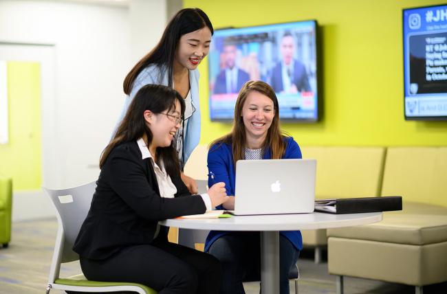 three Carey Business school women students sharing something on a laptop