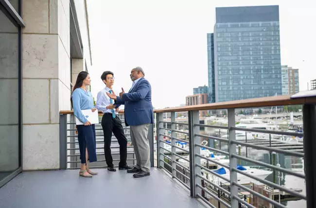 Real estate and infrastructure Professor speaking with two others on a balcony at Carey